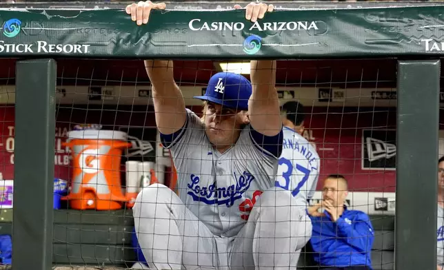 Los Angeles Dodgers starting pitcher Landon Knack stretches while a swarm of bees gathered on the net behind home plate are removed delaying the start of a baseball game between the Los Angeles Dodgers and the Arizona Diamondbacks, Tuesday, April 30, 2024, in Phoenix. (AP Photo/Matt York)