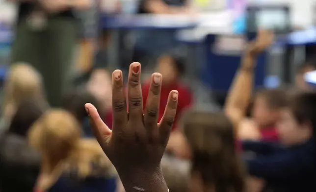 A student raises her hand to contribute in Megan Foster's third grade class, at A.D. Henderson School in Boca Raton, Fla., Tuesday, April 16, 2024. When teachers at the K-8 public school, one of the top-performing schools in Florida, are asked how they succeed, one answer is universal: They have autonomy. (AP Photo/Rebecca Blackwell)