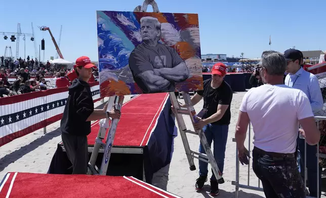 Artist Scott LoBaido, right, looks on as crew members move his painting of Republican presidential candidate former President Donald Trump before a campaign rally in Wildwood, N.J., Saturday, May 11, 2024. (AP Photo/Matt Rourke)