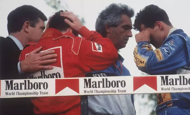 FILE - Italy's Nicola Larini, left, holds his head and Germany's Michael Schumacher, right, wipes a tear from his eyes while talking with Benetton director-general Flavio Briatore, center, on the podium following the San Marino Formula One Grand Prix crash in Imola, Italy, May 1, 1994. The drivers were reacting to the news that the Brazilian driver Ayrton Senna was in critical condition at a Bologna hospital after a crash in the race. Later it was announced that Senna had died after suffering severe head injuries. (AP-Photo/Claudio Luffoli, File)