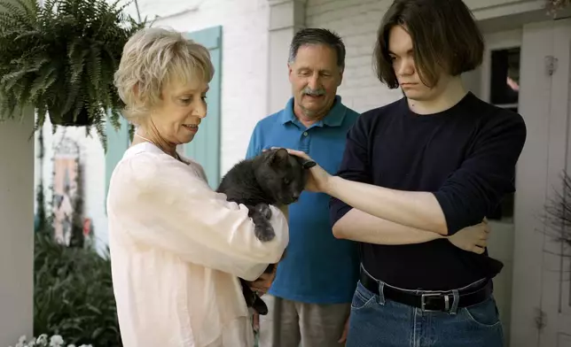 Jesse Fernandez, right, pets the family cat as he visits his former foster parents Jason and Joyce White Friday, May 17, 2024, in Independence, Mo. Fernandez was paid thousands of dollars of Social Security survivor's benefits because of the death of his mother, but by the time he turned 18, the money had all been used by the state of Missouri and Fernandez's relatives to pay for his foster care. (AP Photo/Charlie Riedel)
