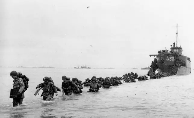 FILE - U.S. reinforcements wade through the surf from a landing craft in the days following D-Day and the Allied invasion of Nazi-occupied France at Normandy in June 1944 during World War II. On D-Day, Charles Shay was a 19-year-old Native American army medic who was ready to give his life — and actually saved many. Now 99, he's spreading a message of peace with tireless dedication as he's about to take part in the 80th celebrations of the landings in Normandy that led to the liberation of France and Europe from Nazi Germany occupation. (Bert Brandt/Pool via AP, File)
