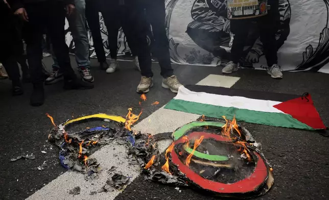 Protesters burn olympic rings on the pavement near a Palestinian flag during the May Day demonstration, Wednesday, May 1, 2024 in Paris. (AP Photo/Thomas Padilla)