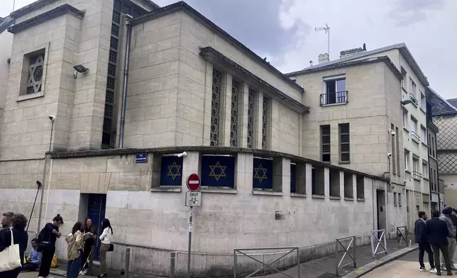 People stand in front the synagogue in Rouen after a man armed with a knife and a metal bar is suspected of having set fire, Friday, May 17, 2024. French police have shot and killed a man armed with a knife and a metal bar who is suspected of having set fire to a synagogue in the Normandy city of Rouen. French police said officers were alerted early Friday morning that smoke was rising from the synagogue and came face to face with the man when they got there. (AP Photo/Oleg Cetinic)
