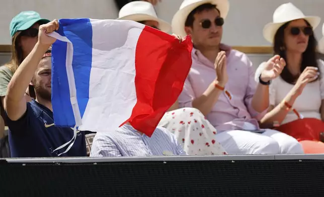 Fans, one waving the French flag, cheer as France's Ugo Humbert plays against Italy's Lorenzo Sonego during their first round match of the French Open tennis tournament at the Roland Garros stadium in Paris, Sunday, May 26, 2024. (AP Photo/Jean-Francois Badias)