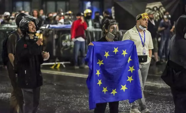 A demonstrator stands with a EU flag in front of police block during an opposition protest against "the Russian law" near the Parliament building in Tbilisi, Georgia, on Wednesday, May 1, 2024. Clashes erupted between police and opposition demonstrators protesting a new bill intended to track foreign influence that the opposition denounced as Russia-inspired. (AP Photo/Zurab Tsertsvadze)