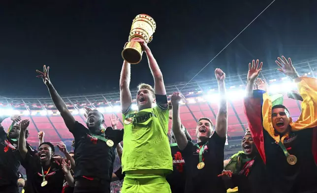 Leverkusen goalkeeper Lukas Hradecky holds up the trophy while his teammates celebrate winning the German Soccer Cup final match between 1. FC Kaiserslautern and Bayer Leverkusen at the Olympic Stadium in Berlin, Germany, Saturday, May 25, 2024. (Federico Gambarini/dpa via AP)