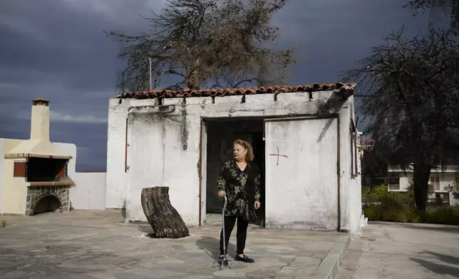 Retiree Chrysoula Renieri, 73, stands outside her house which was burned in July 2023 during a wildfire, in Loutraki, about 82 kilometres (51 miles) west of Athens, Greece, Thursday, April 25, 2024. Greece's fire season officially starts on May 1 but dozens of fires have already been put out over the past month after temperatures began hitting 30 degrees Celsius (86 degrees Fahrenheit) in late March. This year, Greece is doubling the number of firefighters in specialized units to some 1,300, adopting tactics from the United States to try and outflank fires with airborne units scrambled to build breaks in the predicted path of the flames. (AP Photo/Thanassis Stavrakis)