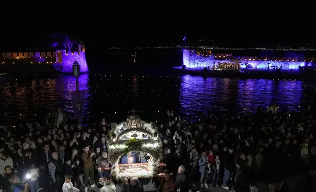 The procession of "Epitaphios", the bier that carries the body of Jesus Christ to his grave, pass the Venetian port, in Nafpaktos town, western Greece, on Good Friday, May 3, 2024. The solemn processions in Greece, with the flower-adorned biers followed by the clergy and the faithful, are often spectacular, especially in places where bier processions from each parish converge into a central square. (AP Photo/Thanassis Stavrakis)