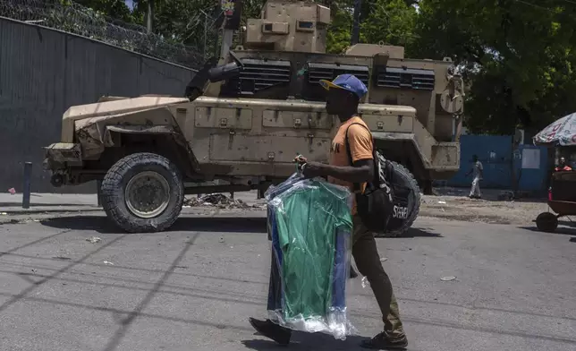 a man carries dry cleaning past an armored police vehicle in Port-au-Prince, Haiti, Sunday, April 28, 2024. (AP Photo/Ramon Espinosa)