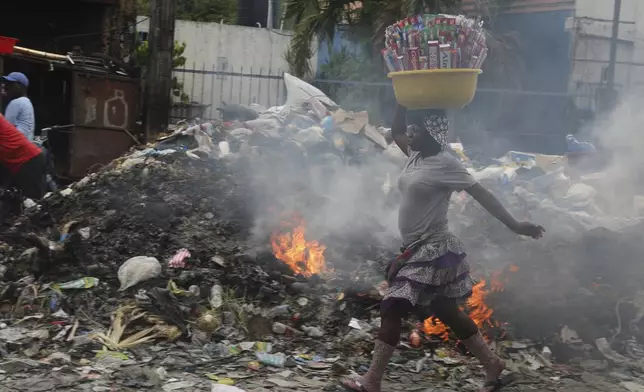 A street vendor walks past a pile of burning trash, in Port-au-Prince, Haiti, Tuesday, April 30, 2024. (AP Photo/Odelyn Joseph)