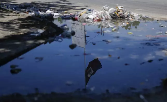A Haitian flag is reflected in a puddle, lined with trash, in the Champ de Mars area of Port-au-Prince, Haiti, Tuesday, April 30, 2024. (AP Photo/Ramon Espinosa)
