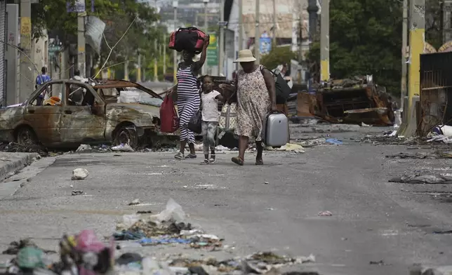 Residents walk past a burnt car blocking the street as they evacuate the Delmas 22 neighborhood to escape gang violence in Port-au-Prince, Haiti, Thursday, May 2, 2024. (AP Photo/Ramon Espinosa)