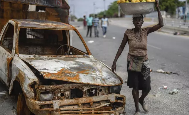 A fruit vendor walks by a burned car in the Delmas district of Port-au-Prince, Haiti, Thursday, May 2, 2024. (AP Photo/Ramon Espinosa)