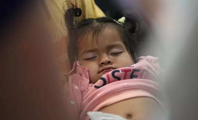 One-year-old Triana Cataleya San Juan sleeps on the lap of her father, Robinson, as he listens during an orientation session for recent immigrants, Monday, May 20, 2024, in Denver. (AP Photo/David Zalubowski)