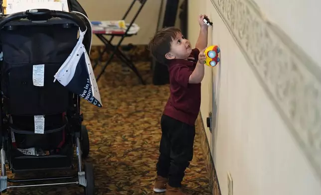 Two-year-old Rodrigo Guacapan runs his toy vehicles on the wall as his parents attend an orientation session for recent immigrants Monday, May 20, 2024, in Denver. (AP Photo/David Zalubowski)