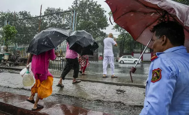 People holding umbrellas cross a railway line in Kolkata, India, as rain continues after cyclone Remal made a landfall near Bangladesh-India border, Monday, May 27, 2024. (AP Photo/Bikas Das)