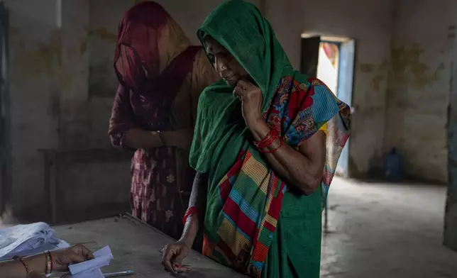 Voters wait as a polling official checks their names before allowing them to cast their vote during the third round of voting in the six-week-long general election in Agra, Uttar Pradesh, India, Tuesday, May 7, 2024. (AP Photo/Altaf Qadri)