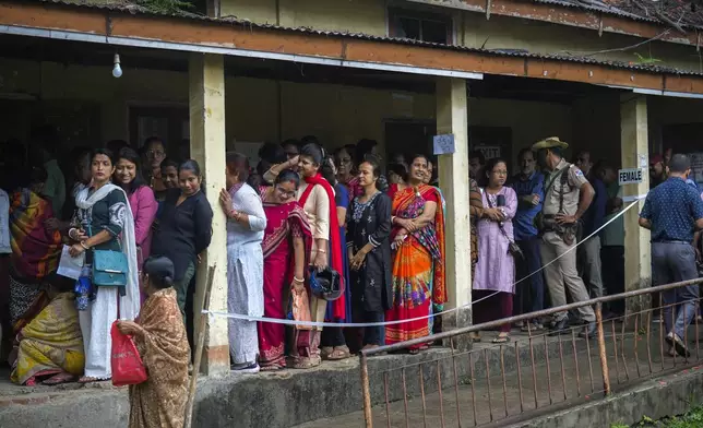 A security person stands guard as voters stand in queue to cast their votes in a polling station during the third phase of general election in Guwahati, India, Tuesday, May 7, 2024. (AP Photo/Anupam Nath)