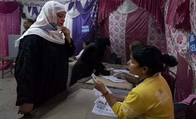 A polling official inspects the identity card of a Muslim voter as she arrives to cast her vote in the sixth round of polling in India's national election in New Delhi, India, Saturday, May 25, 2024. (AP Photo/Altaf Qadri)