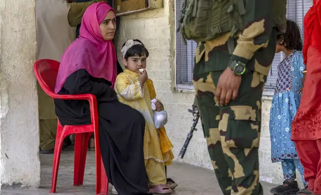 A paramilitary soldier stands guard as a Kashmiri woman sits with her daughter waiting for her turn to vote in the sixth round of polling in India's national election in Kanelwan, south of Srinagar, Indian controlled Kashmir, Saturday, May 25, 2024. (AP Photo/Dar Yasin)
