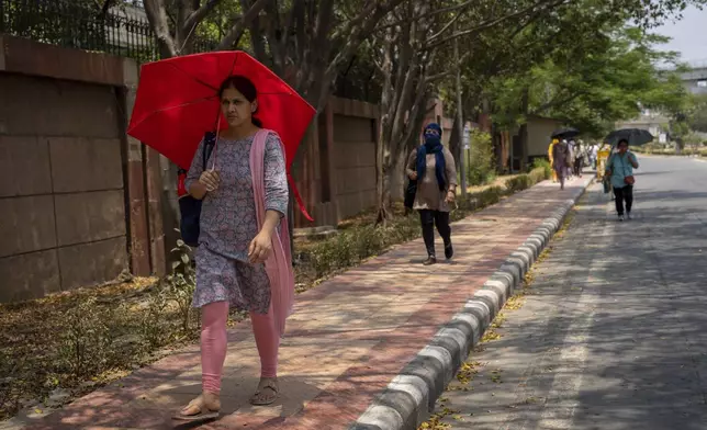 A polling official carries an umbrella to protect herself from the heat as she walks towards electronic voting machines distribution centre on the eve of the sixth round of multi-phase national elections in New Delhi, India, Friday, May 24, 2024. (AP Photo/Altaf Qadri)