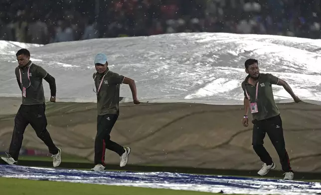 Groundsmen run to cover the ground as rain interrupts the Indian Premier League cricket match between Punjab Kings and Royal Challengers Bengaluru in Dharamshala, India, Thursday, May 9, 2024. (AP Photo /Ashwini Bhatia)