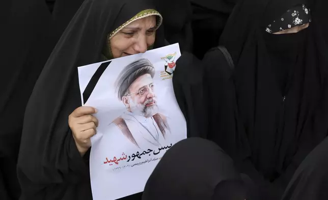 In this photo released by the Iranian Presidency Office, a woman mourns as she holds a poster of President Ebrahim Raisi in a funeral ceremony for him and his companions who were killed in a helicopter crash on Sunday in a mountainous region of the country's northwest, in the city of Tabriz, Iran, Tuesday, May 21, 2024. The sign in the poster reads in Farsi: "Martyr President" (Iranian Presidency Office via AP)