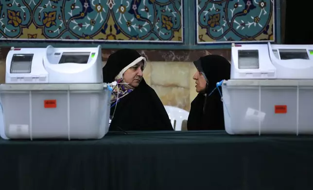 Staff members of a polling station talk during the parliamentary runoff elections in Tehran, Iran, Friday, May 10, 2024. Iranians voted Friday in a runoff election for the remaining seats in the country's parliament after hard-line politicians dominated March balloting. (AP Photo/Vahid Salemi)