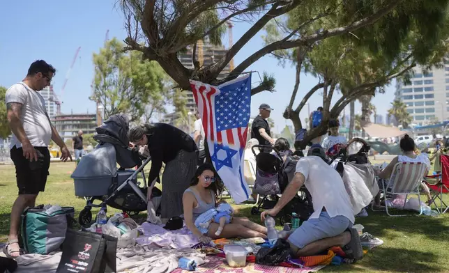 A woman holds her baby as she sits next to a flag displaying Israeli and U.S. national symbols together during Israel's Independence Day celebrations in Tel Aviv, Tuesday, May 14, 2024. Israelis are marking 76 years since Israel's creation. (AP Photo/Ohad Zwigenberg).