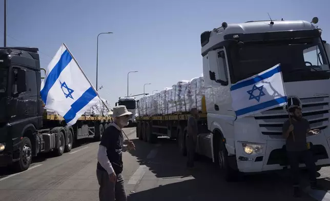 Holding Israeli flags people stand in front of trucks carrying humanitarian aid as they try to stop them to enter in the Gaza Strip in an area near the Kerem Shalom border crossing between Israel and Gaza, in southern Israel, in Kerem Shalom, Thursday, May 9, 2024. (AP Photo/Leo Correa)