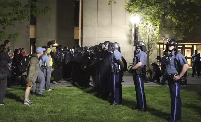 Students and supporters, left, stand in front of members of law enforcement early Wednesday, May 8, 2024, on the University of Massachusetts Amherst campus, in Amherst, Mass. Police moved in Tuesday night to break up an encampment at the school, in what appeared in video to be an hours-long operation as dozens of police officers in riot gear systematically tore down tents and took protesters into custody. The protesters established the tent encampment to demonstrate against the war in Gaza. (Kalinka Kornacki via AP)