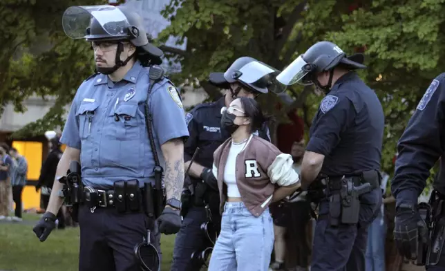Members of law enforcement place a person in handcuffs, Tuesday, May 7, 2024, on the University of Massachusetts Amherst campus, in Amherst, Mass. Police moved in Tuesday night to break up an encampment at the school in what appeared in video to be an hours-long operation as dozens of police officers in riot gear systematically tore down tents and took protesters into custody. The protesters established the tent encampment to demonstrate against the war in Gaza. (Kalinka Kornacki via AP)