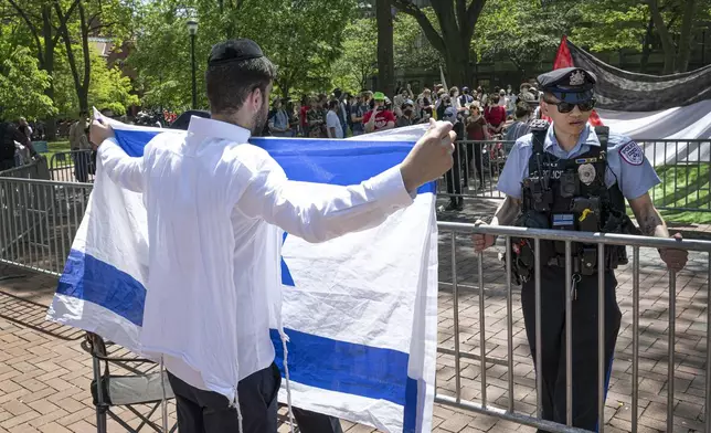 A pro-Israel supporter waves the Israeli flag in front of a police officer and a pro-Palestinian camp at the University of Pennsylvania encampment Thursday, May 2, 2024, in Philadelphia. (Jose F. Moreno/The Philadelphia Inquirer via AP)