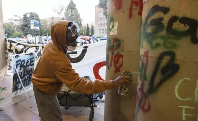 A demonstrator sprays graffiti on a building on the UCLA campus, Wednesday, May 1, 2024, in Los Angeles. (AP Photo/Ethan Swope)
