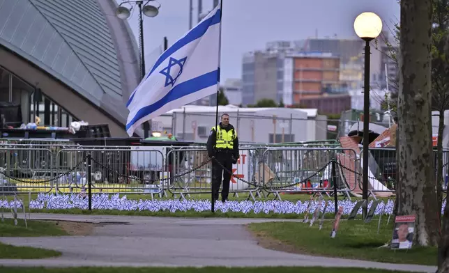 A Police officer stands behind a display of Israeli flags beside the pro-Palestinian encampment that police raided and dismantled at MIT, before dawn Friday, May 10, 2024, in Cambridge, Mass. (AP Photo/Josh Reynolds)