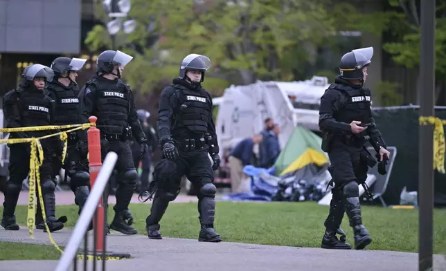 A line of police in riot gear walk past a garbage truck being loaded with the remains of the pro-Palestinian encampment at MIT, which police raided before dawn Friday, May 10, 2024, in Cambridge, Mass. (AP Photo/Josh Reynolds)