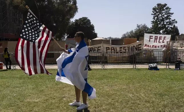 Draped in an Israeli flag, a pro-Israel supporter walks with an American flag near the pro-Palestinian encampment on the University of California, Los Angeles (UCLA) campus in Los Angeles, Tuesday, April 30, 2024. (AP Photo/Jae C. Hong)