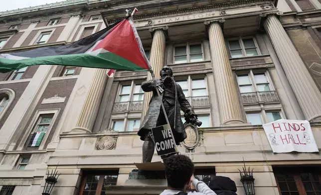 A student protester parades a Palestinian flag outside the entrance to Hamilton Hall on the campus of Columbia University, Tuesday, April 30, 2024, in New York. Early Tuesday, dozens of protesters took over Hamilton Hall, locking arms and carrying furniture and metal barricades to the building. Columbia responded by restricting access to campus. (AP Photo/Mary Altaffer, Pool)