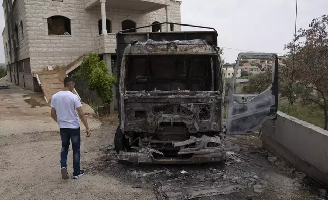 Fatahi Mohammad, 20, walks past his family's truck that was torched during an attack by Israel settlers last month, in the West Bank village of Duma, Tuesday, April 30, 2024. (AP Photo/Nasser Nasser)