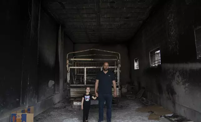 Ibrahim Dawabsha, 34, holds hands with his daughter Ghena, 3 while posing for a picture in front of his truck, at the garage of the family house, that was torched during an attack by Israel settlers last month, in the West Bank village of Duma, Tuesday, April 30, 2024. (AP Photo/Nasser Nasser)