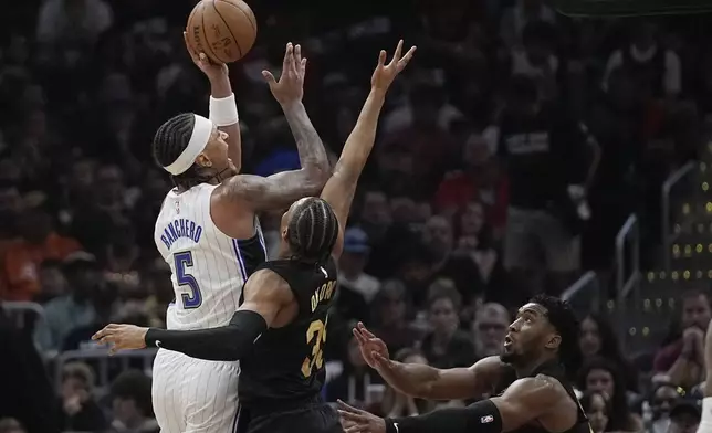 Orlando Magic forward Paolo Banchero (5) shoots over Cleveland Cavaliers forward Isaac Okoro, center, and guard Donovan Mitchell, right, in the first half of Game 7 of an NBA basketball first-round playoff series Sunday, May 5, 2024, in Cleveland. (AP Photo/Sue Ogrocki)