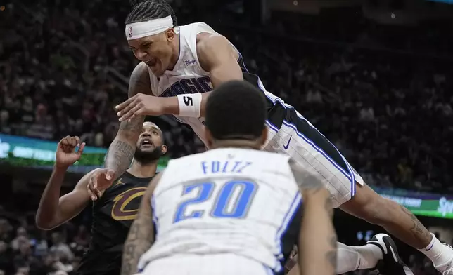Orlando Magic forward Paolo Banchero, center, falls between Cleveland Cavaliers forward Evan Mobley, left, and teammate Markelle Fultz (20) after committing an offensive foul on Isaac Okoro in the second half of Game 7 of an NBA basketball first-round playoff series, Sunday, May 5, 2024, in Cleveland. (AP Photo/Sue Ogrocki)
