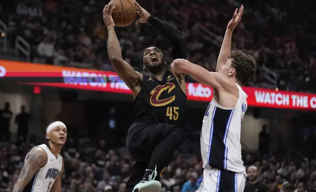 Cleveland Cavaliers guard Donovan Mitchell (45) shoots between Orlando Magic forward Paolo Banchero (5) and forward Franz Wagner, right, in the first half of Game 7 of an NBA basketball first-round playoff series Sunday, May 5, 2024, in Cleveland. (AP Photo/Sue Ogrocki)