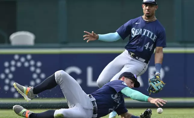 Seattle Mariners left fielder Dylan Moore, bottom, with Mariners center fielder Julio Rodriguez (44) backing him up, dives for a single by Washington Nationals' Keibert Ruiz during the seventh inning of a baseball game, Saturday, May 25, 2024, in Washington. (AP Photo/John McDonnell)