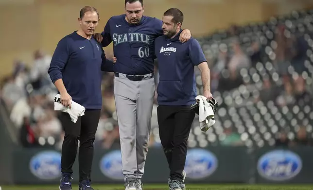 Seattle Mariners relief pitcher Tayler Saucedo (60) walks off the field with trainers after sustaining an injury during the eighth inning of a baseball game against the Minnesota Twins, Tuesday, May 7, 2024, in Minneapolis. (AP Photo/Abbie Parr)