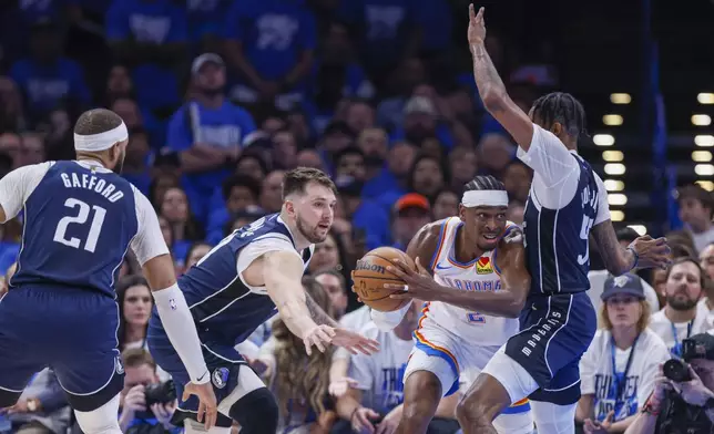 Oklahoma City Thunder guard Shai Gilgeous-Alexander, center, tries to pass the ball to a teammate as Dallas Mavericks center Daniel Gafford (21), guard Luka Doncic, second from left, and forward Derrick Jones Jr. defend during the first half of Game 1 of an NBA basketball second-round playoff series, Tuesday, May 7, 2024, in Oklahoma City. (AP Photo/Nate Billings)