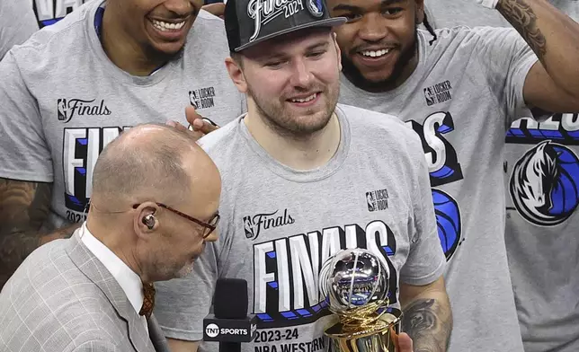 Dallas Mavericks guard Luka Doncic, center, holds the MVP trophy as he is surrounded by teammates as announcer Ernie Johnson Jr., left, interviews Doncic after Game 5 of the Western Conference finals in the NBA basketball playoffs against the Minnesota Timberwolves, Thursday, May 30, 2024, in Minneapolis. The Mavericks won 124-103, taking the series 4-1 and moving on to the NBA Finals. (AP Photo/Matt Krohn)