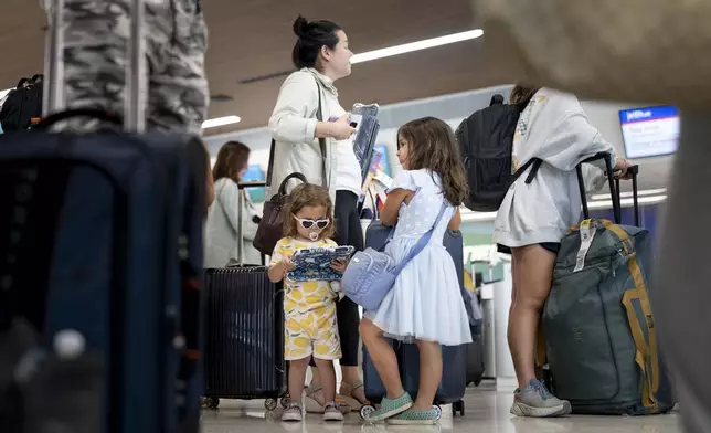 Citra Gonzalez, 3, left, and her sister Camellia Gonzalez, 6, wait in line with their mother Deanna Oswald, above, to check in for their flight at the Nashville international Airport, Thursday, May 23, 2024, in Nashville, Tenn. A record number of Americans are expected to travel over the 2024 Memorial Day holiday. (AP Photo/George Walker IV)