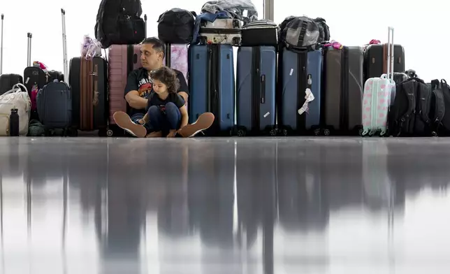 Samuel Tadros and his daughter Serenity 3, sit with the family's bags after their flight to New York was cancelled at the Nashville international Airport Thursday, May 23, 2024, in Nashville, Tenn. A record number of Americans are expected to travel over the 2024 Memorial Day holiday. (AP Photo/George Walker IV)